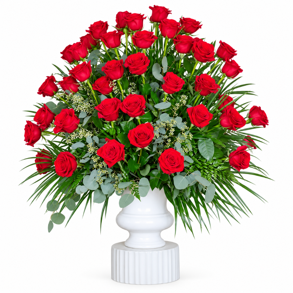 Funeral arrangement of red roses with fancy greenery  in a white urn.