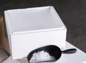 White styrofoam EPS cooler box with lid and black scoop filled with dry ice pellets on white surface